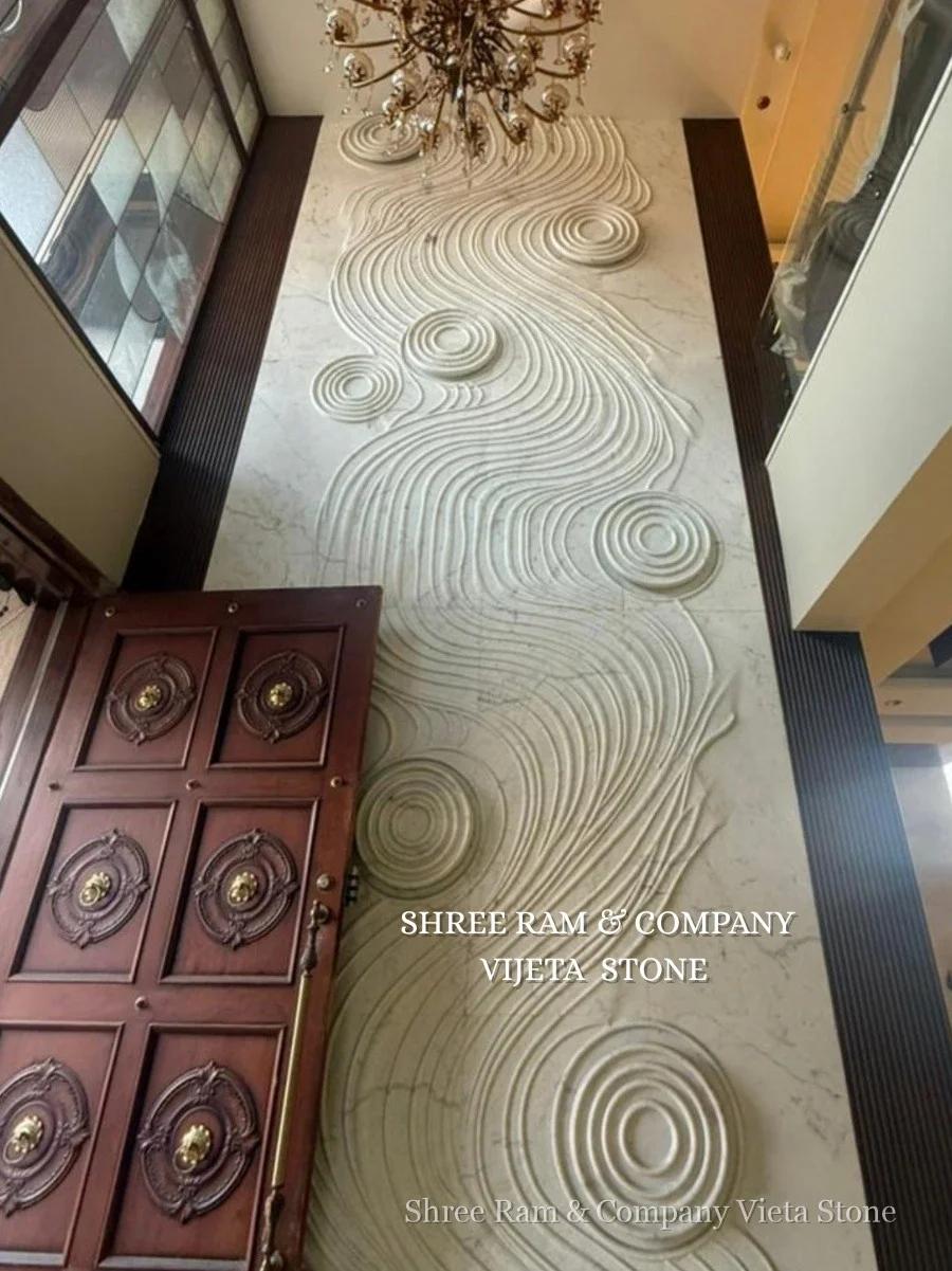 Vertical zen ripple water wave grooved marble wall cladding soaring to ceiling beside ornate hand-carved wooden entrance door - Shree Ram and Company Vijeta Stone
